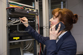 Pretty technician talking on phone while fixing server