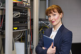 Pretty technician smiling at camera beside open server holding tablet pc