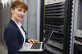 Pretty technician using laptop while working on server smiling at camera