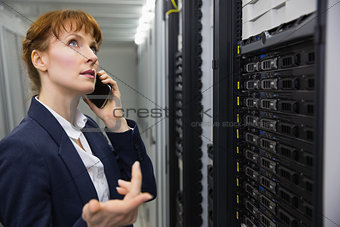 Pretty technician talking on phone while looking at server
