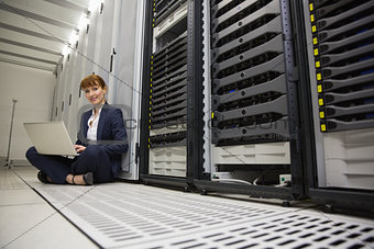 Technician sitting on floor beside server tower using laptop