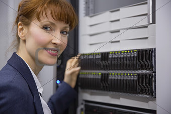 Pretty technician smiling at camera beside server tower