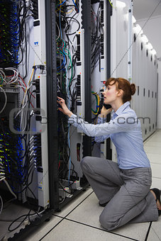 Serious technician talking on phone while analysing server