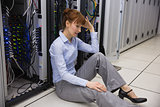 Stressed technician sitting on floor beside open server
