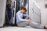 Stressed technician sitting on floor beside open server