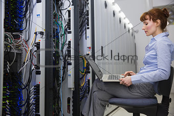 Technician sitting on swivel chair using laptop to diagnose servers