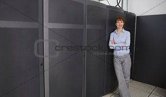 Pretty technician smiling at camera beside server towers