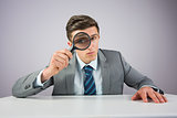 Businessman sitting at desk with magnifying glass
