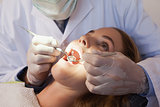 Dentist examining a patients teeth in the dentists chair under bright light
