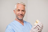 Dentist in blue scrubs holding mouth model