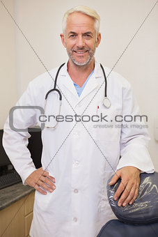 Dentist smiling at camera beside chair