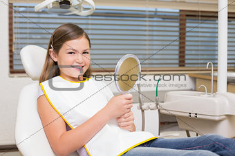 Little girl holding mirror in dentists chair