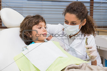 Pediatric dentist showing little boy in chair the drill