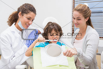 Pediatric dentist showing little boy how to brush teeth with his mother