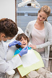 Pediatric dentist examining a little boys teeth with his mother