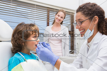Pediatric dentist examining a little boys teeth with his mother watching
