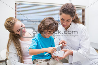 Pediatric dentist showing little boy how to brush teeth with his mother
