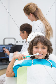 Little boy smiling at camera with mother and dentist in background