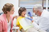 Pediatric dentist examining a little boys teeth with his mother watching