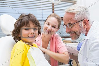Little boy smiling at camera with mother and dentist beside him