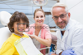 Little boy smiling at camera with mother and dentist beside him