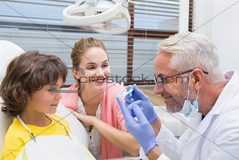 Pediatric dentist showing little boy a toothbrush with his mother
