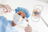 Dentist in surgical mask and cap holding dental tools over patient