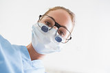 Dentist in surgical mask and dental loupes looking down over patient