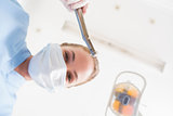 Dentist in surgical mask holding dental drill over patient