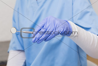 Dentist in blue scrubs holding angled mirror