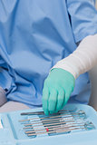 Dentist in blue scrubs picking up tools