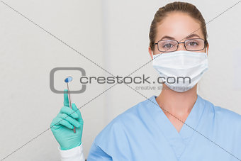 Dentist in blue scrubs holding angled mirror looking at camera