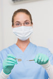 Dentist in blue scrubs holding tools looking at camera