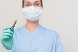 Dentist in blue scrubs holding drill looking at camera
