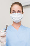 Dentist in blue scrubs holding drill looking at camera