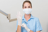 Dental assistant in mask looking at camera pulling on gloves