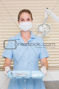 Dental assistant in mask holding tray of tools