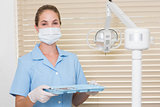Dental assistant in blue holding tray of tools