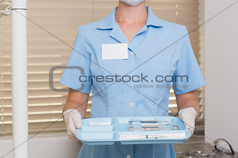 Dental assistant in blue holding tray of tools