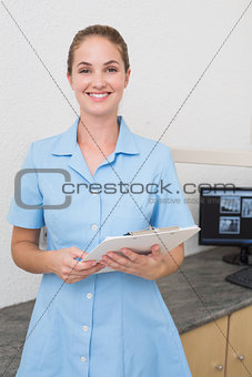 Smiling dental assistant looking at camera holding clipboard