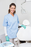 Dentist in blue scrubs smiling at camera beside chair