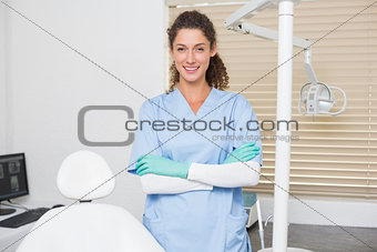 Dentist in blue scrubs smiling at camera beside chair