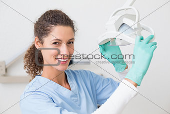 Dentist in blue scrubs smiling at camera beside light
