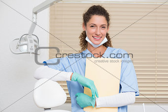 Dentist in blue scrubs smiling at camera holding file