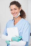 Dentist in blue scrubs smiling at camera holding clipboard