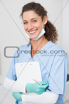 Dentist in blue scrubs smiling at camera holding clipboard