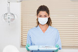 Dentist in blue scrubs holding tray of tools