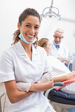 Dental assistant smiling at camera with dentist and patient behind