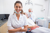 Dental assistant smiling at camera with dentist and patient behind