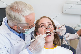 Dentist examining a patients teeth in the dentists chair with assistant